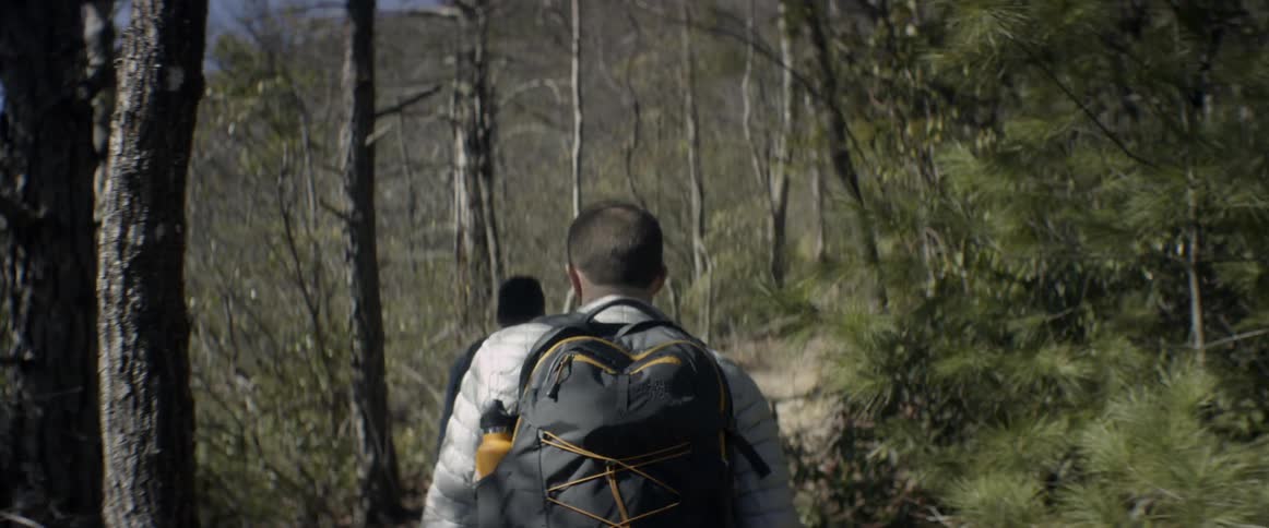 Two men wearing backpacks hike a trail in a forest