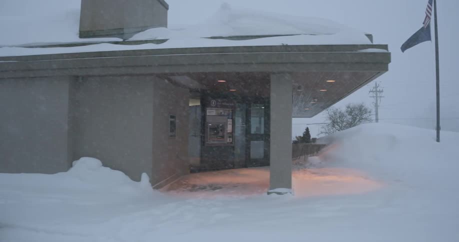 Filmed from a passing car during a heavy blizzard the camera glides past deep snowdrifts and a flagpole to reveal the warmly lit entrance of a bank branch in alaska