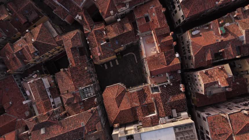 This birdseye view captures a dense cluster of historic buildings featuring warm terracottatiled roofs and narrow alleywaysthe camera slowly rotates and pulls back revealing a hidden rectangular courtyard nestled in the heart of the architectural