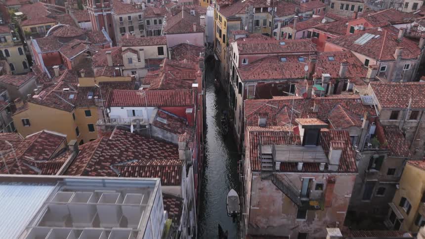 An aerial drone shot descends over the densely packed terracotta rooftops of venice revealing a narrow canal winding between the buildings below