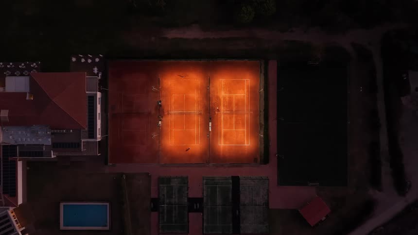 Illuminated tennis courts viewed from above in a sports complex at night