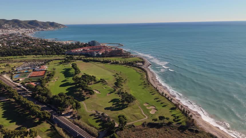 Aerial view of a seaside golf course with an urban complex and the ocean alongside