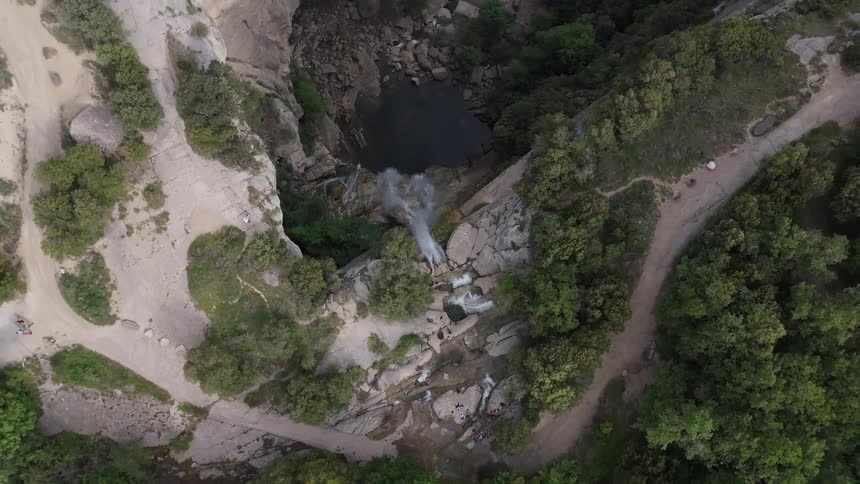 Waterfall flows over rocks between trails and dense vegetation seen from above