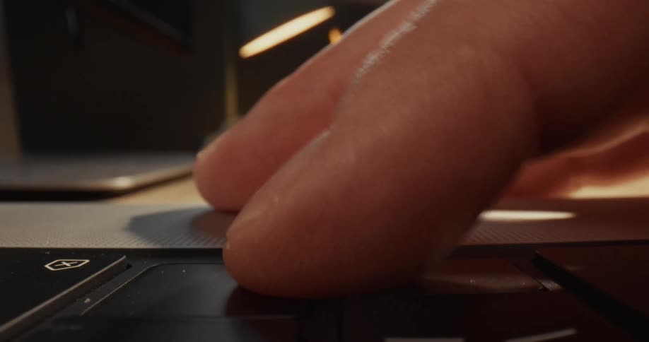 A close view of a man using a finger to press the enter key on a laptop keyboard in a room with warm lighting