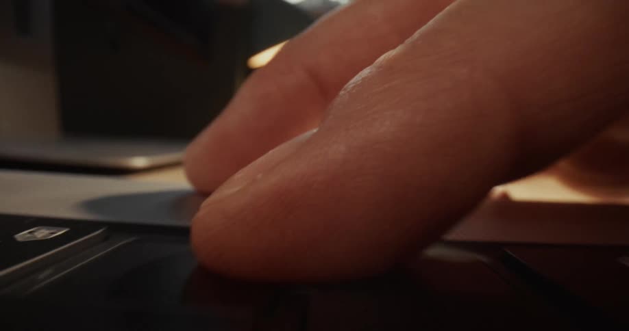 A closeup shot captures a persons hand interacting with a laptop keyboard in a dimly lit environment the camera focuses on the fingertips pressing down on individual keys as the user types or navigates