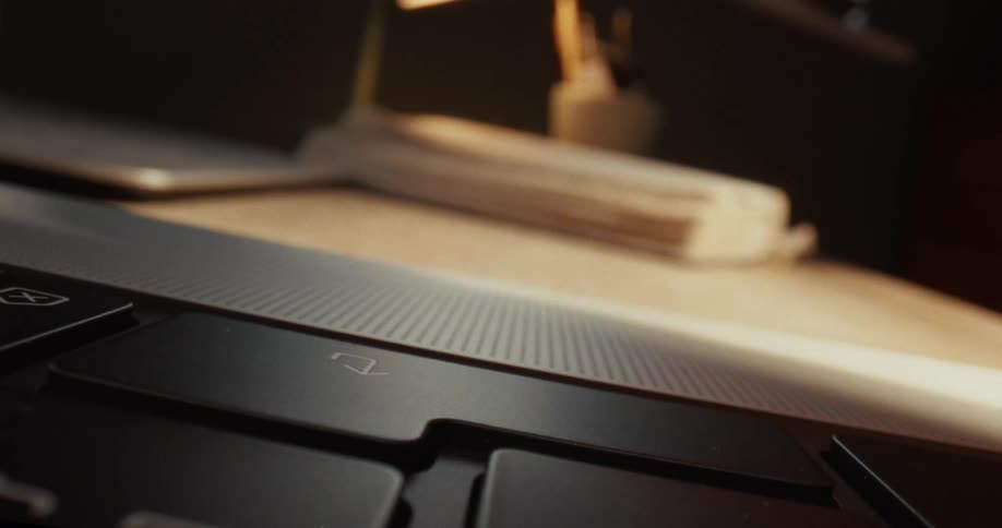 An extreme closeup captures a finger repeatedly tapping the down arrow key on a sleek black laptop the surrounding desk softly blurred by warm light