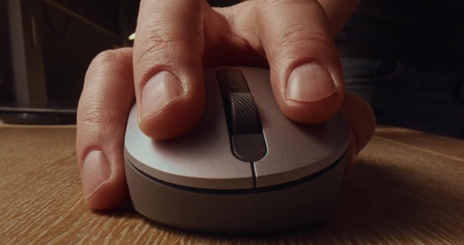 Hand moving a computer mouse across a wooden table and clicking