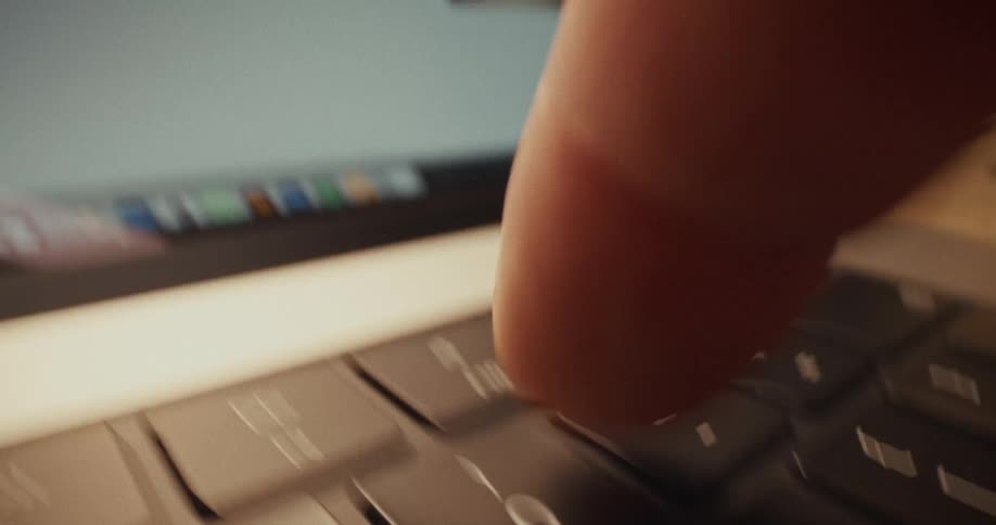 A close up view shows a persons finger pressing keys on a laptop keyboard