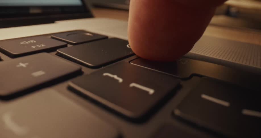 An extreme closeup shot shows a persons finger hovering and then pressing down on a laptop trackpadas the camera pulls back slightly the edge of the laptop screen and the wooden surface of a desk come into view