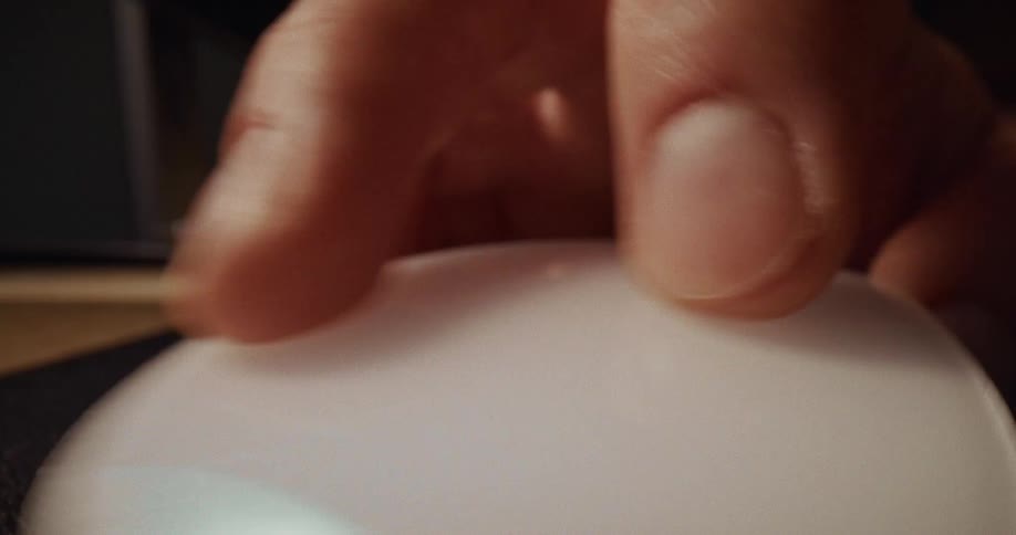 A closeup shot captures a finger making contact with the smooth curved surface of a white computer mouse the lowangle perspective emphasizes the texture of the skin and the soft warm lighting surrounding the device