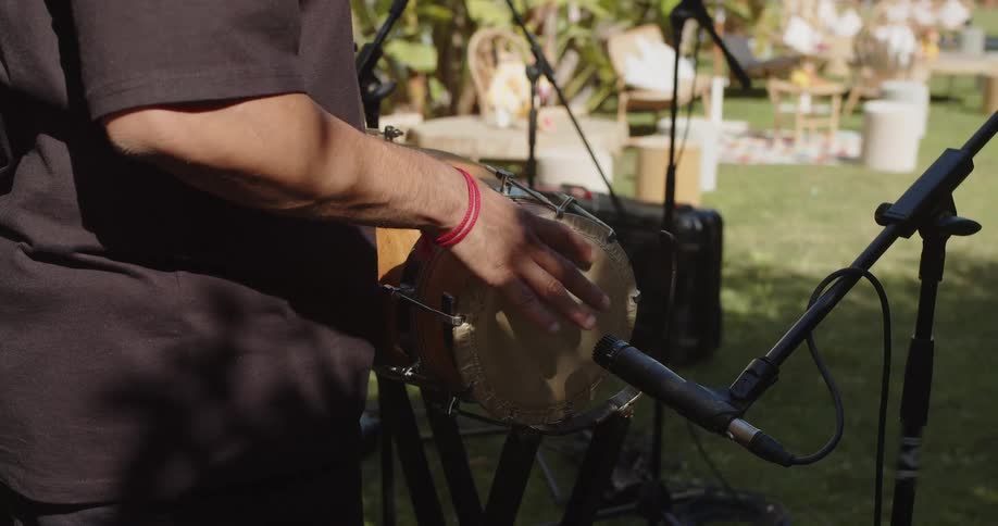 Musician playing a percussion instrument with a microphone during an outdoor performance