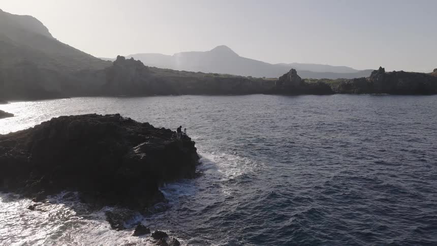 Coastal rock formation surrounded by the sea with mountains in the background