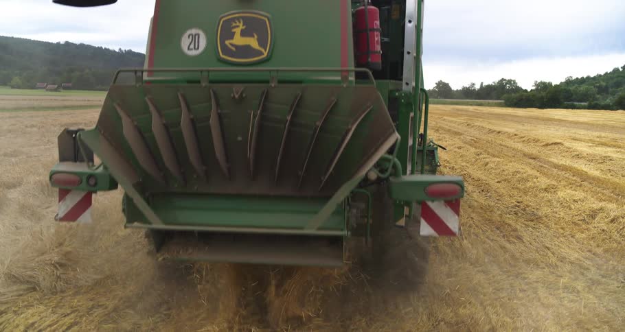 A green john deere combine harvester moves through a golden field processing crops during a harvest the machine leaves a trail of scattered straw behind it as it travels across the vast agricultural landscape