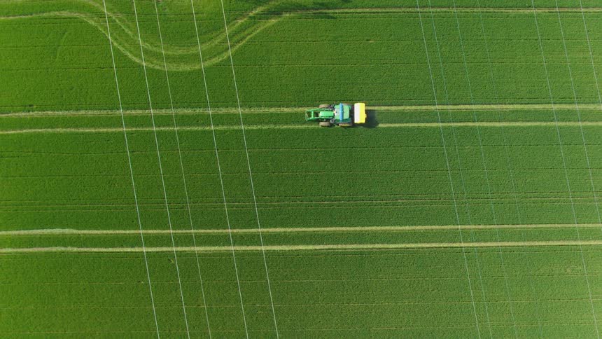 Agricultural vehicle moving across a green field with parallel lines seen from above