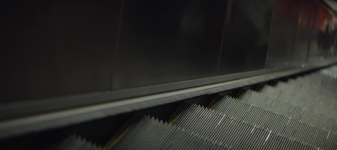 Metal wall of a moving escalator reflects people