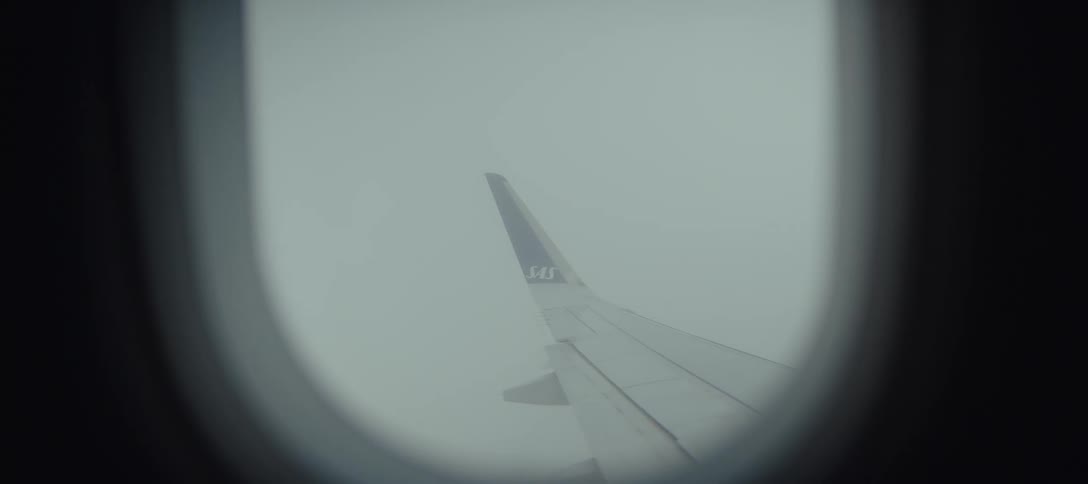 An airplane wing with the sas logo is visible through a window as the aircraft flies through thick grey cloudsthe camera remains steady on the wingtip while the dense mist outside creates a hazy and somber atmosphere