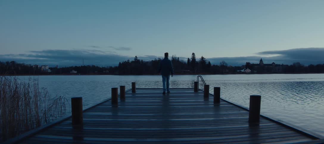 Person walking along a wooden pier toward a lake at dusk