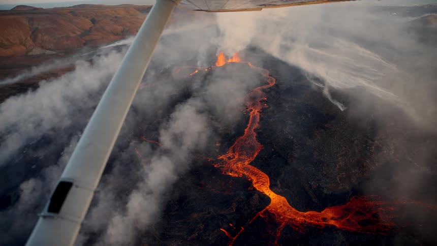Aerial footage shows a river of molten lava flowing from a volcanic eruption the scene is captured from a small plane flying over the smoky dark landscape