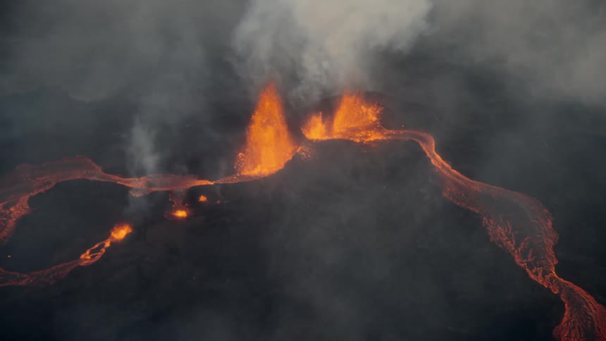 Molten hot lava from an erupting volcano splashes into the air and flows across the land