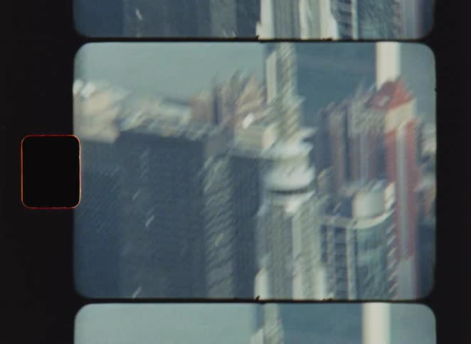 Vintage film footage captured on an eight millimeter camera shows a high view of a tall white skyscraper in a city with other office buildings and a river in the background under daylight