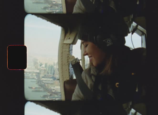 Female passenger of an aircraft flying over a waterfront city smiles out the open door