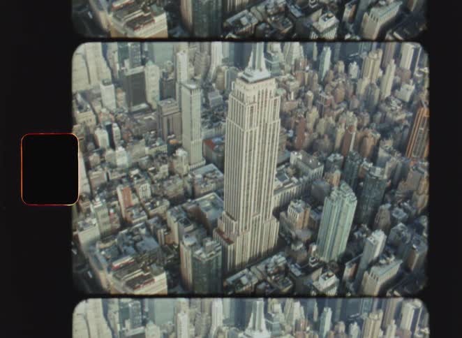 Vintage film footage captured on an eight millimeter camera shows a high view of the empire state building rising above other skyscrapers and city blocks in new york city with a river in the distance