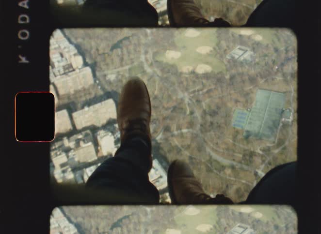 The persons feet dangle out of the flying aircraft
