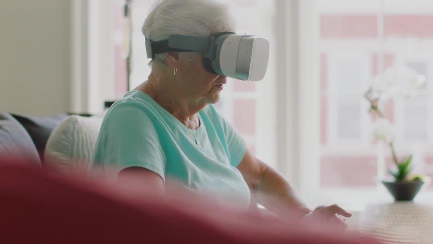 Older woman sitting on couch wearing virtual reality headset is looking around