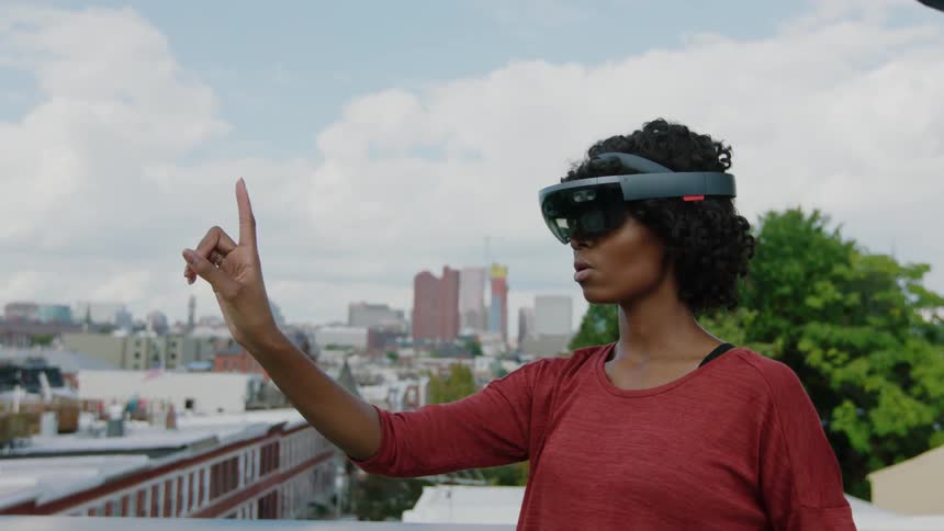 Woman outside on rooftop is wearing virtual reality headset and moving her hand