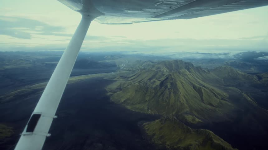 The plane is flying very high above the green mountains