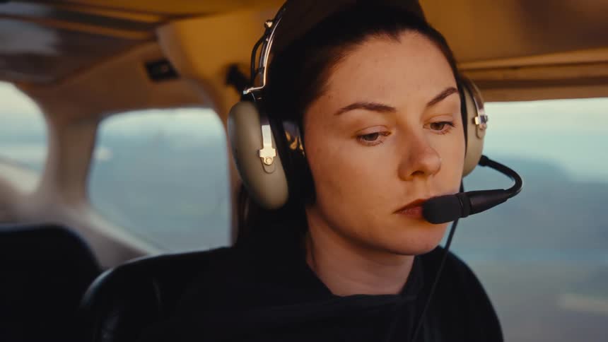 Woman pilot looks around and speaks into her microphone as she flies a small airplane