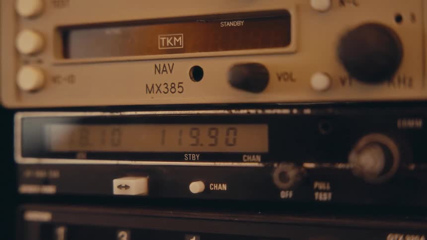 A close view of aircraft radio equipment with glowing digital displays and various control knobs inside a cockpit