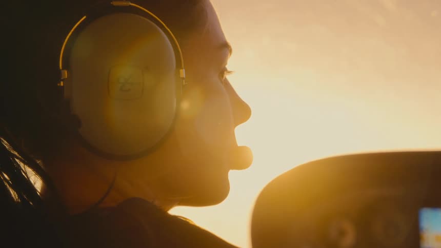 A woman wearing a headset gazes ahead from an airplane cockpit illuminated by the warm glow of a golden sunset