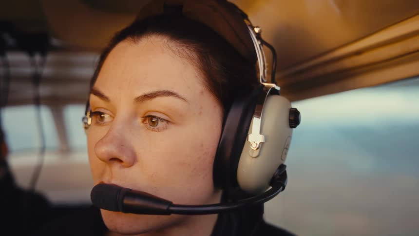 Woman with headset observes landscape through window during flight in aircraft cabin