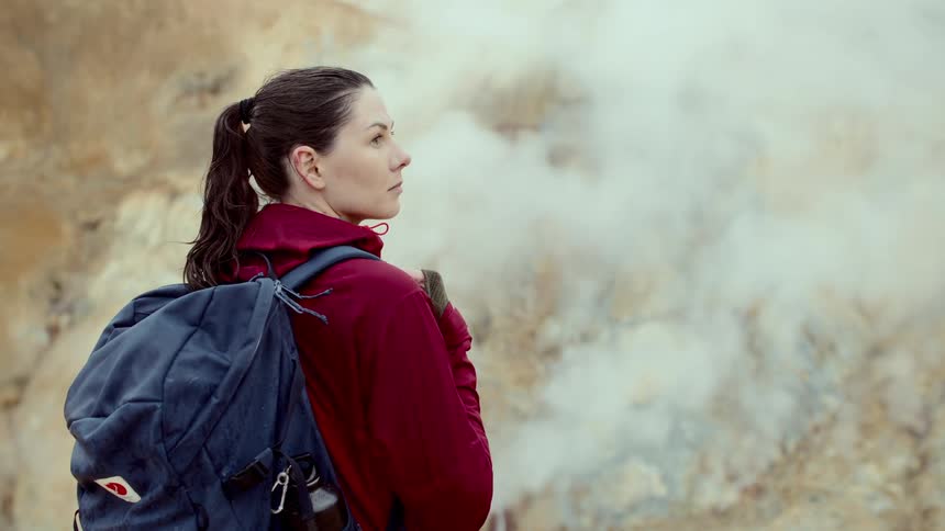 Female backpacker stands looking while vapor rises nearby