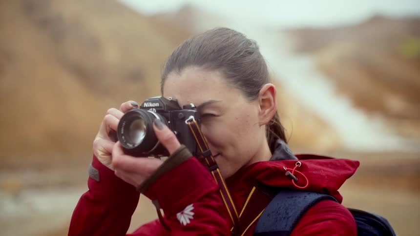 Person in red jacket photographing mountainous landscape with water stream using nikon camera