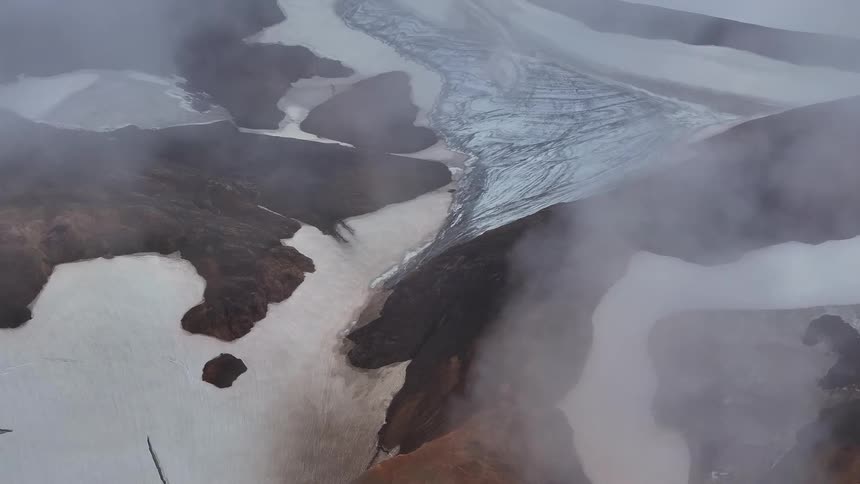 Clouds drifts over a rugged snow dusted mountain landscape in an aerial view