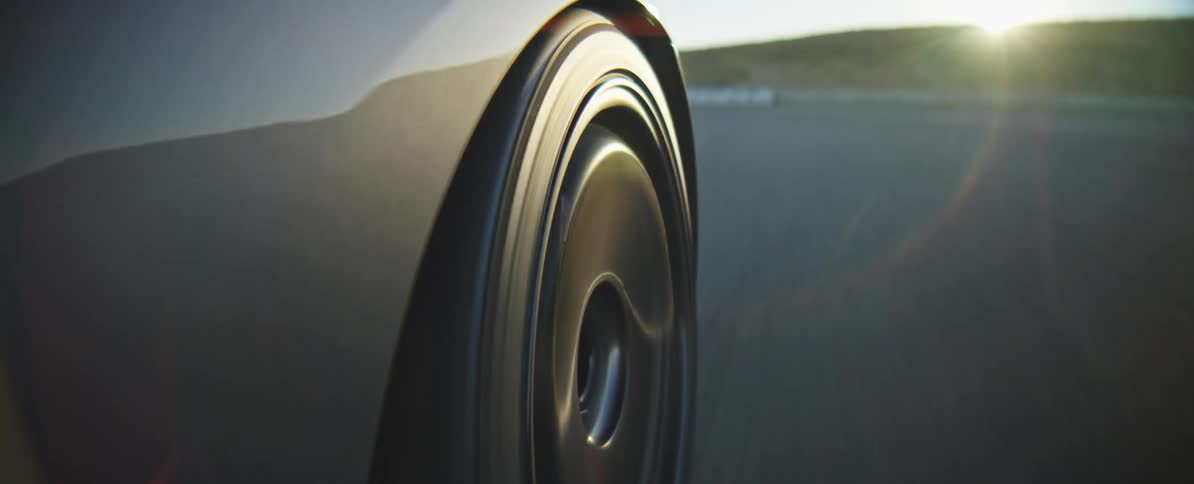 A close view of a black car wheel spinning at high speed on an asphalt road with bright golden sunlight and lens flare in the background during a clear day