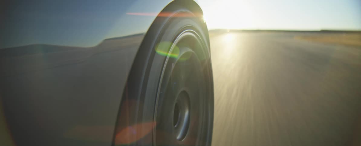 A close view of a car wheel spinning as the vehicle travels quickly along a paved track while the sun shines brightly