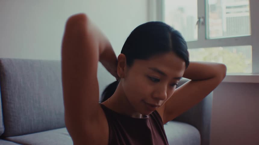 A close view shows a woman with dark hair pulling her hair back into a ponytail while sitting in a room