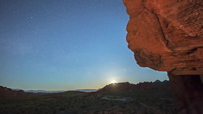 Illuminated rock formation stands out against the starry sky at dawn in a mountainous region