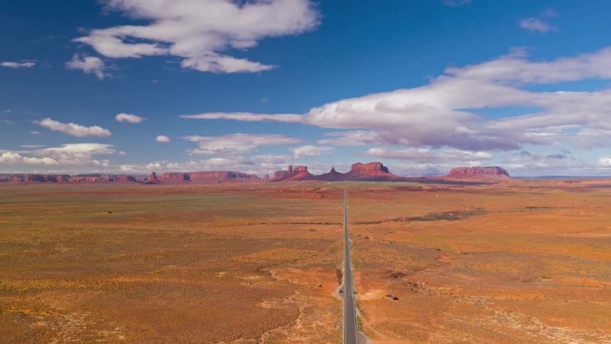 Traffic moves on a desert highway with butte and mesa red rock formations across the distant landscape