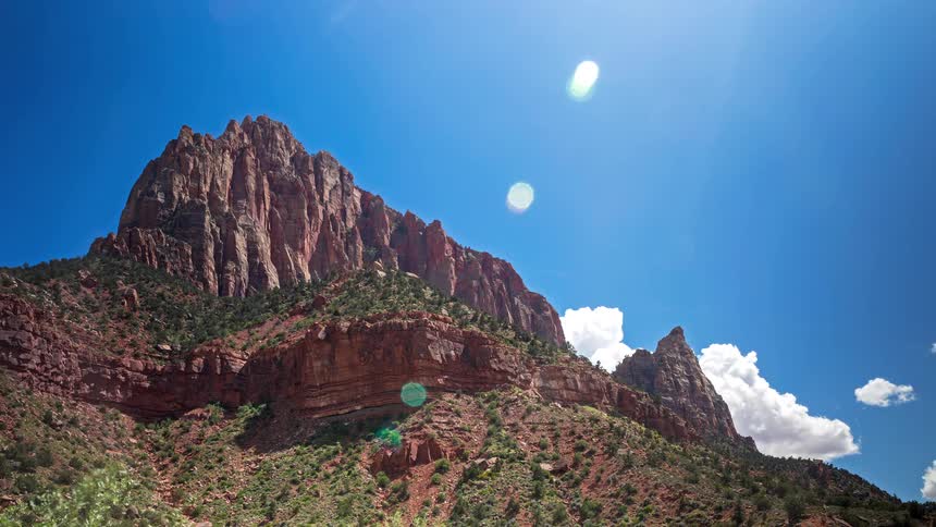 Clouds move behind a mountain with plants and vegetation on the slope