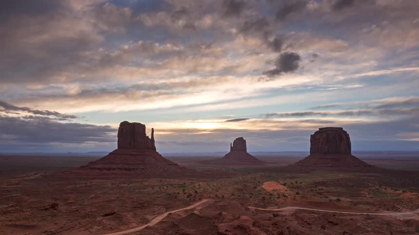 Traffic moves on a road through the desert with buttes and red rock formations across the landscape
