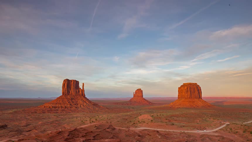 Mesa and buttes across the desert landscape as clouds move overhead and cars travel on the road