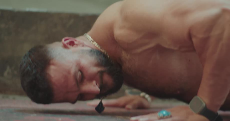 A close view of a muscular man with a beard as he performs pushups on a colorful rug while wearing several rings and a digital watch