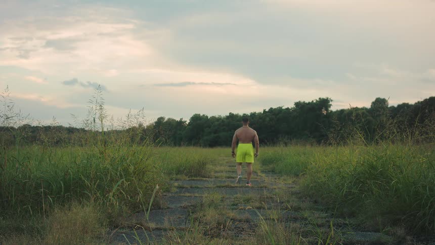 Muscular man walking along a path in an open area surrounded by vegetation