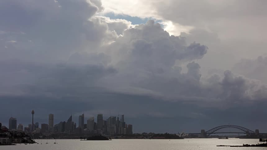 A city skyline with a bridge over a lake in the foreground as boats move by on a cloudy midday