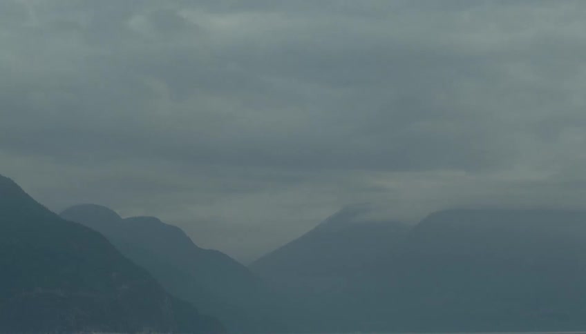 A mountain range stretches across the wilderness under a cloudy sky the peaks fading softly into a foggy atmosphere that settles between the ridges