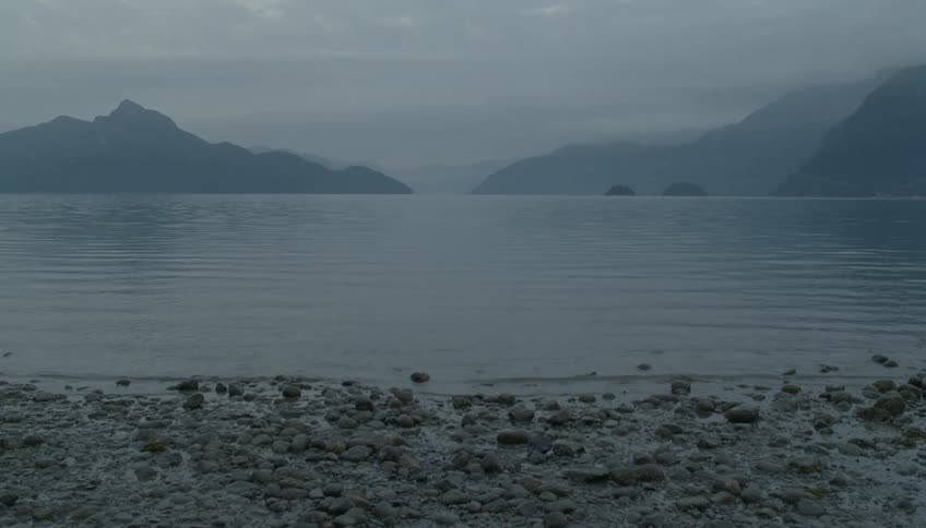 Waves flow away from the fog covered mountains and towards the pebble strewn shore